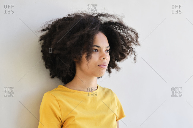 Curly hair student looking away while leaning on white wall