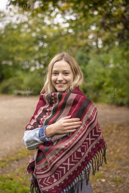 Smiling woman wrapped in scarf at park during autumn