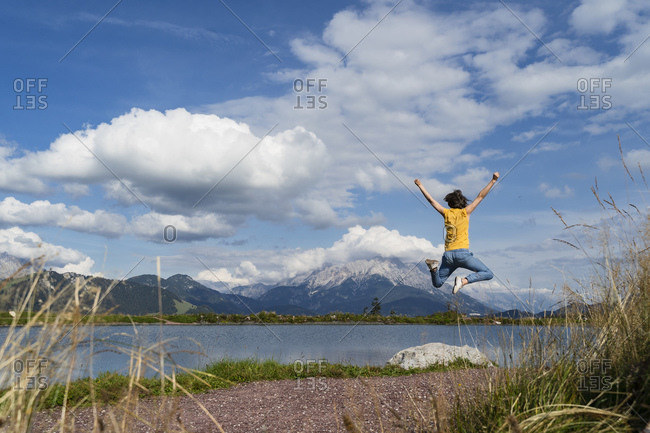 Young woman jumping on shore of alpine lake in spring