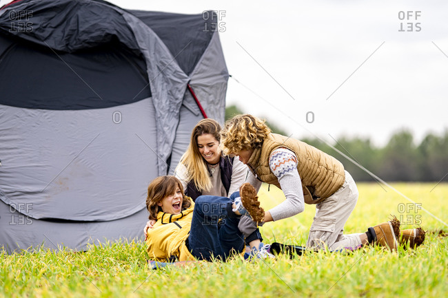 Three siblings playing on grass in front of pitched tent
