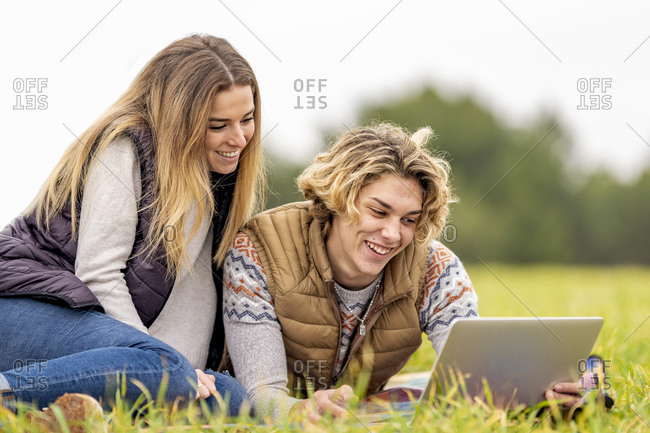 Brother and sister lying together on grass with digital tablet