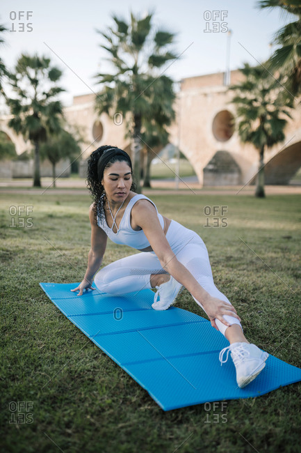 Female athlete exercising on mat over grass in public park