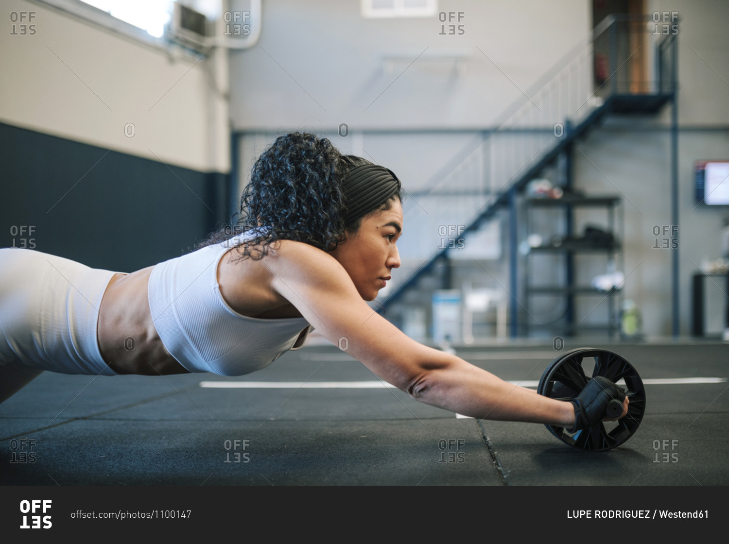 Confident sportswoman training with abdominal toning wheel in gym