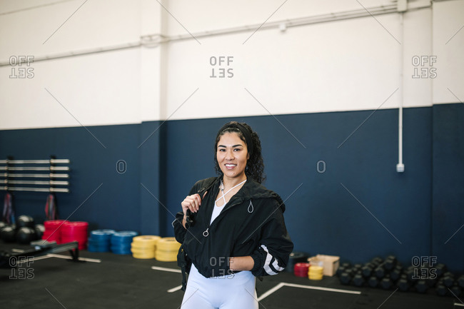 Smiling sportswoman with hands in pockets carrying backpack at gym