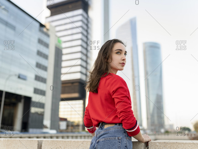 Attractive woman looking away while leaning on railing by buildings