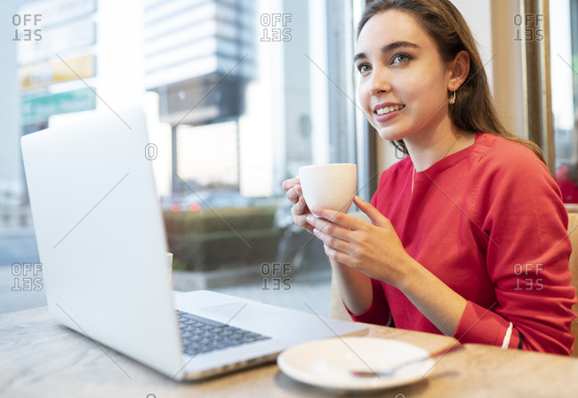 Beautiful woman with coffee cup and laptop sitting in cafe