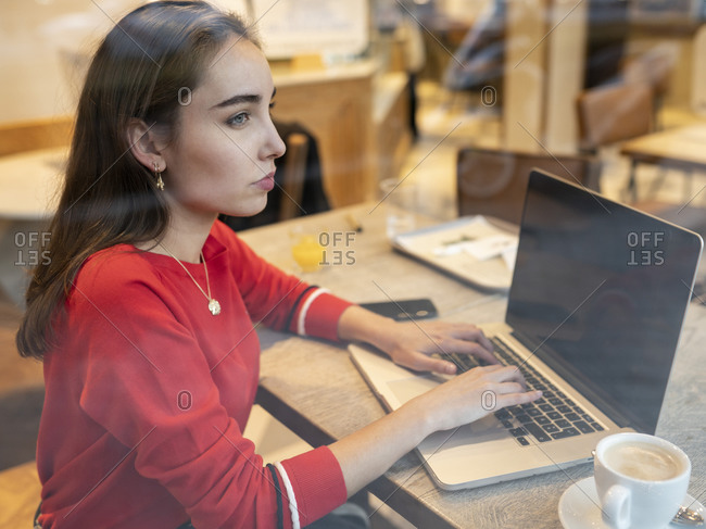 Thoughtful woman with laptop seen through glass of cafe
