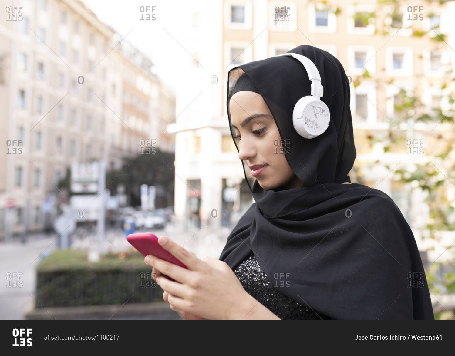 Portrait of young beautiful woman wearing hijab and headphones using
