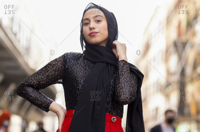 Portrait of young woman wearing black hijab posing outdoors with hand on hip