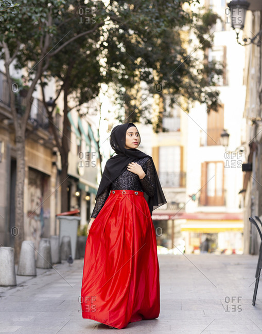 Portrait of young woman wearing hijab and long skirt walking along sidewalk