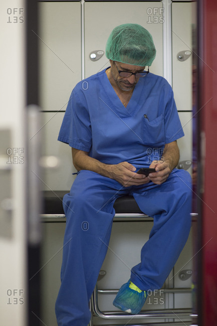 Male surgeon in surgical cap using smart phone at hospital
