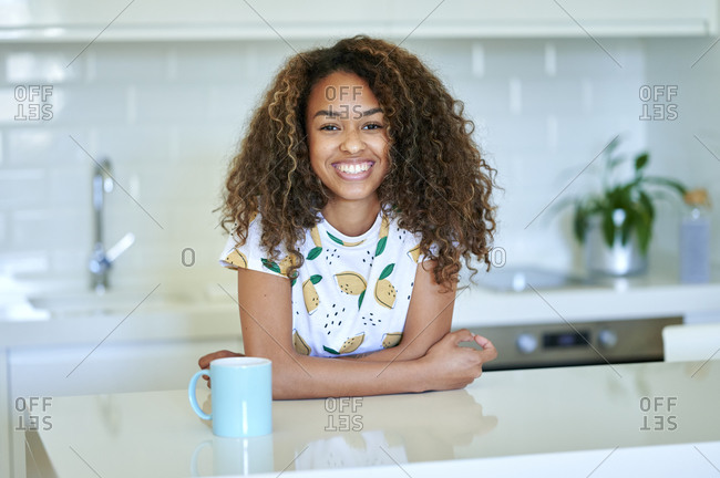 Smiling young afro woman with coffee cup leaning on counter in kitchen
