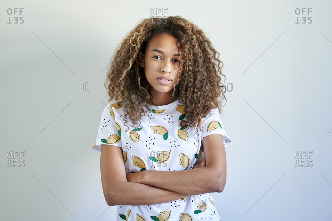 Confident young woman with arms crossed against white wall
