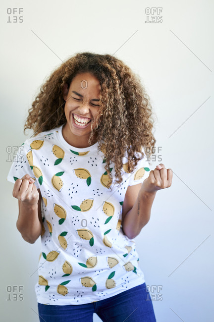 Laughing young woman punching fist in air against white wall