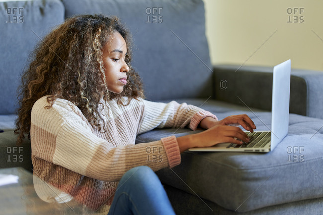 Young woman with curly hair using laptop in living room at home