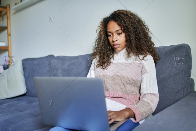 Young afro woman using laptop with concentration on sofa at home