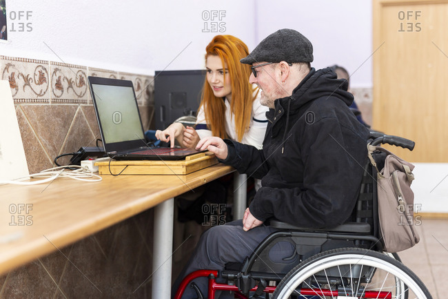 Young female nurse teaching laptop to disabled man at rehabilitation center