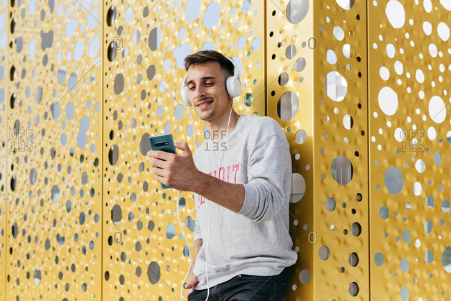 Smiling man listening music while leaning on wall
