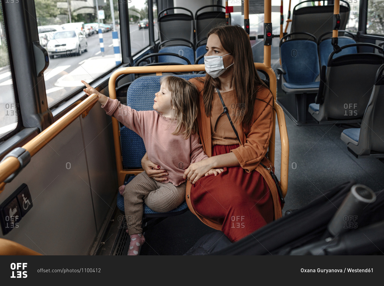 Mother with cute daughter pointing at window while traveling by bus during COVID-19