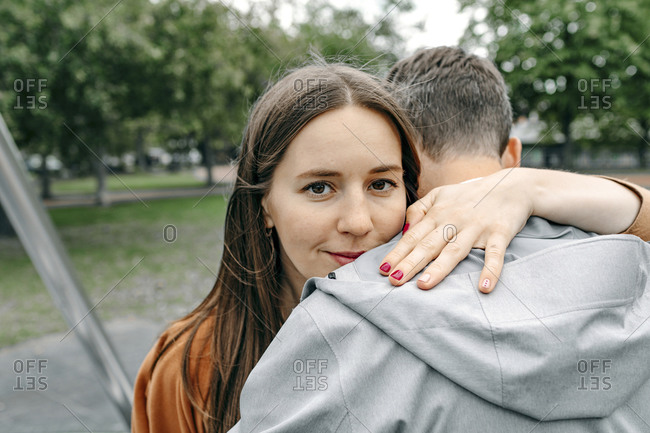 Smiling girlfriend embracing boyfriend in public park