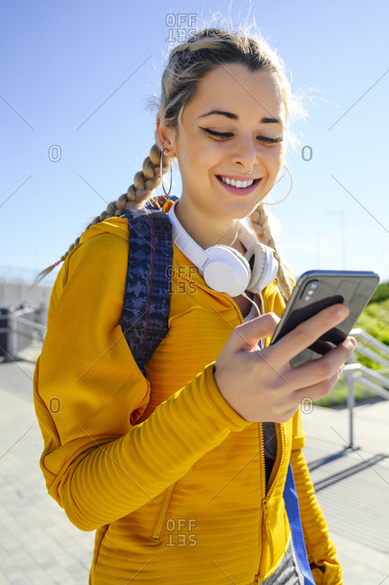 Young sportswoman with backpack using mobile phone while standing against sky