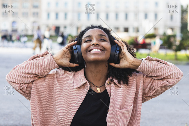 Smiling young with eyes closed listening music through headphones