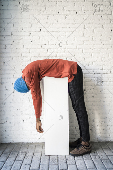 Mid adult man bending over pedestal against white brick wall