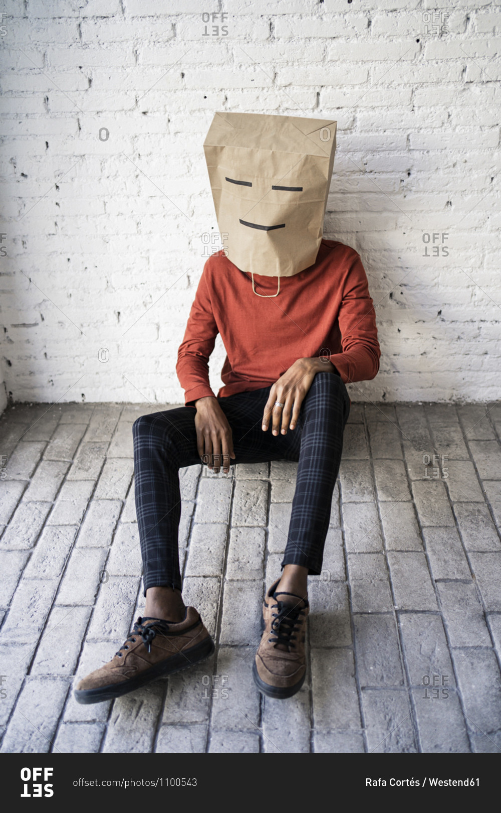 Man wearing brown paper bag on head against white brick wall stock ...