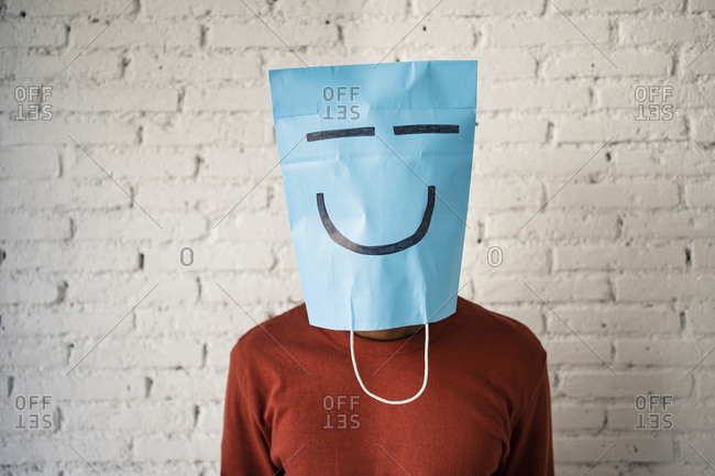 Mid adult man wearing blue paper bag on face against white brick wall