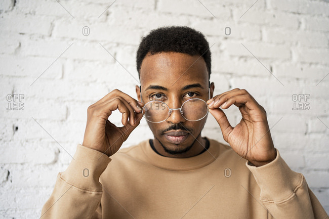 Mid adult man holding eyeglasses against white brick wall