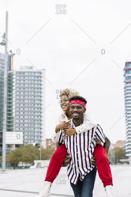 Playful man piggybacking woman while walking in city