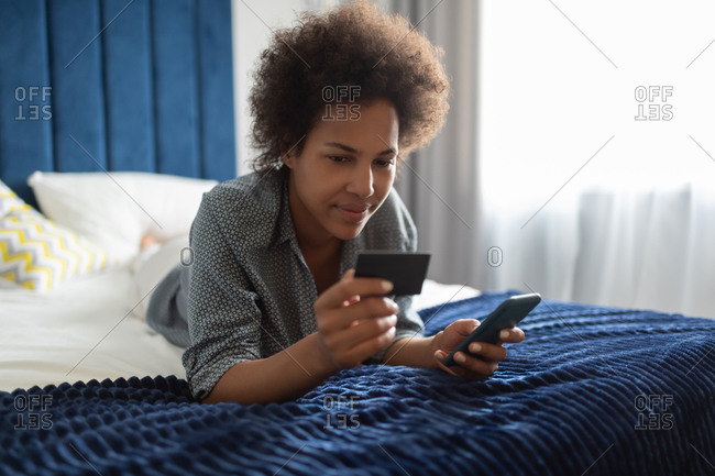 African American woman making online purchases on bed