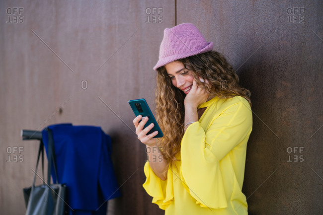 Young female using smartphone near wall and scooter