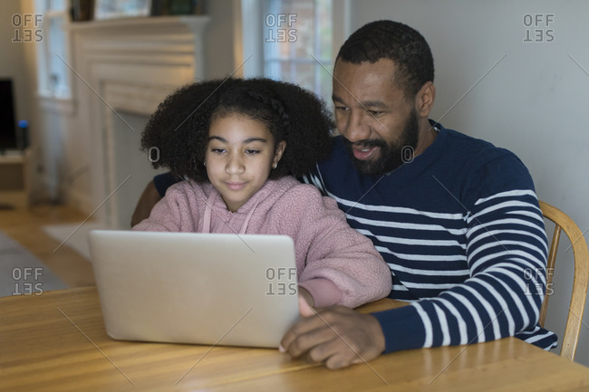 An African-American father and bi-racial tween daughter on laptop