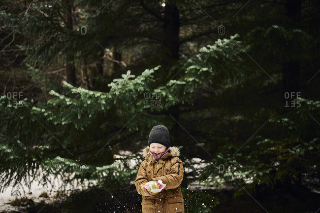 Happy child making snowball near fir tree in forest