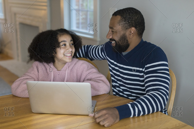 An African-American father and tween daughter smile at each other