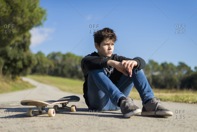 Handsome teen male with a skateboard sitting on asphalt road