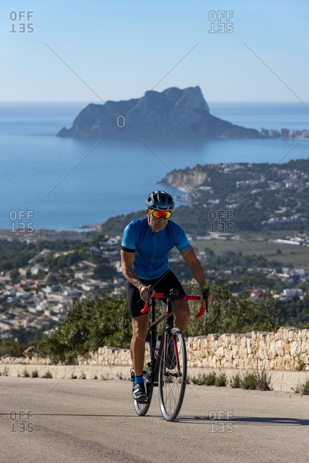 Cyclist climbing Cumbre del Sol hill with view of mediterranean sea.