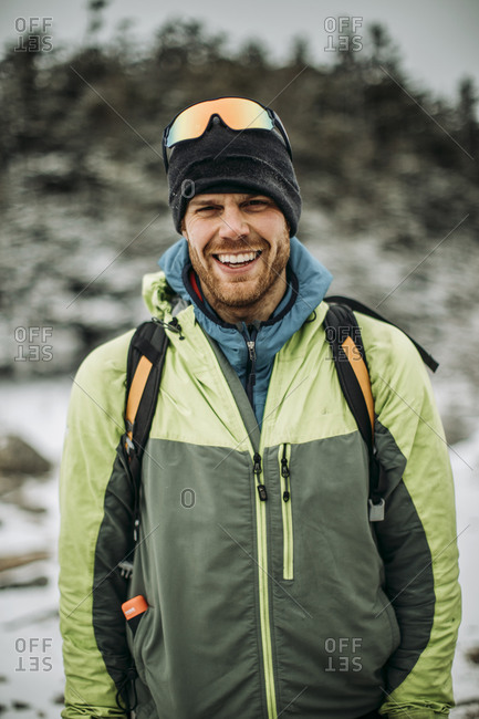 Portrait of smiling man in winter jacket and hat wearing backpack