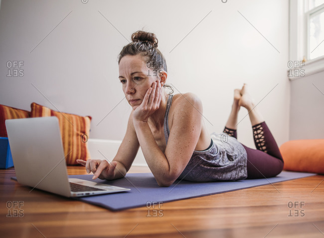Woman in yoga clothes relaxes on floor indoors on laptop computer