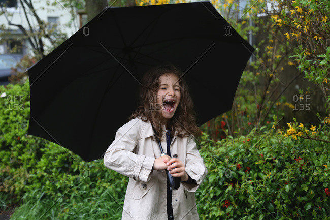 A girl with long curly hair under an umbrella smiles broadly.