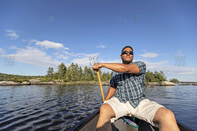 African man paddles canoe along rocky shore of pond in Maine