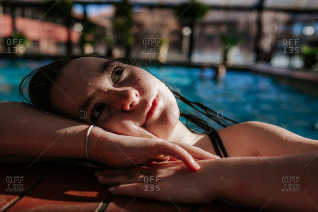 Happy tween girl resting on the side of a swimming pool