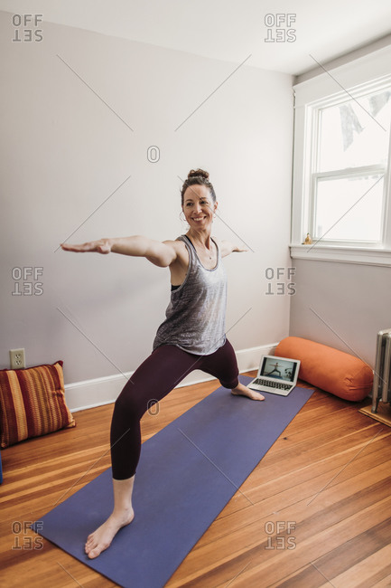 smiling woman in yoga clothes does yoga with help of laptop computer