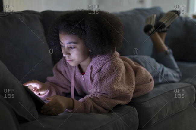 Ten year-old bi-racial girl working on her ipad while lying on sofa