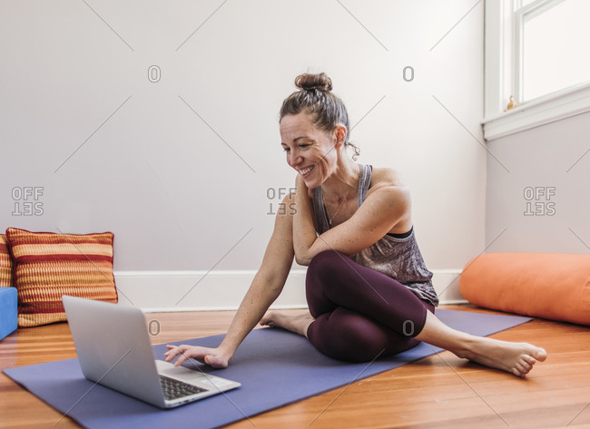 Smiling woman in yoga clothing uses laptop to workout in her home