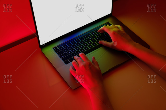Female hands on a modern laptop keyboard in brightly lit red bac