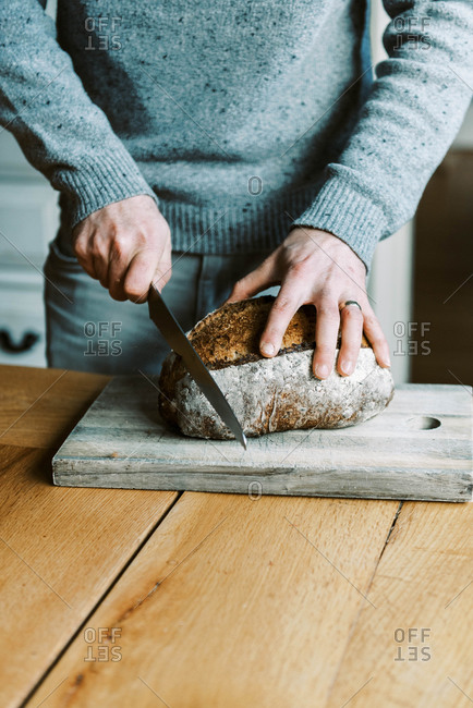 Hands of a man holding and cutting a rustic sourdough bread with knife