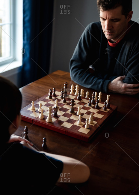 Father and son sitting at a table indoors playing a game of chess.