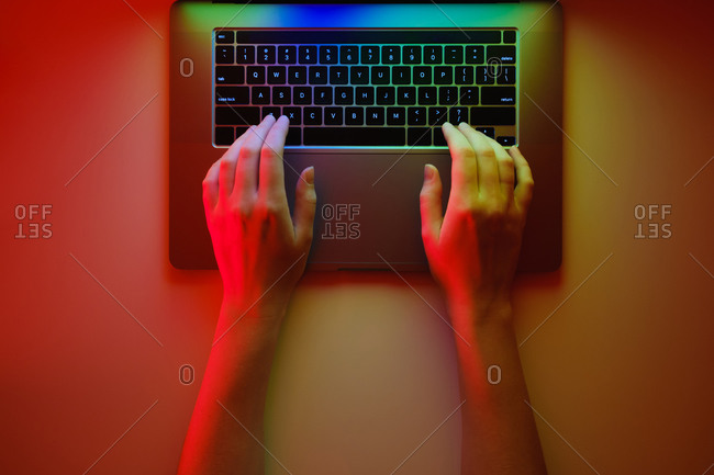 Hands on a modern laptop keyboard, top view and bright lit red b